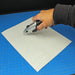 A person using a heavy-duty utility knife to cut a custom shape out of a flexible steel sheet on a blue hobby cutting mat.