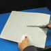Demonstration of a hobbyist cutting a custom shape from a flexible steel sheet using standard household scissors on a blue cutting mat.
