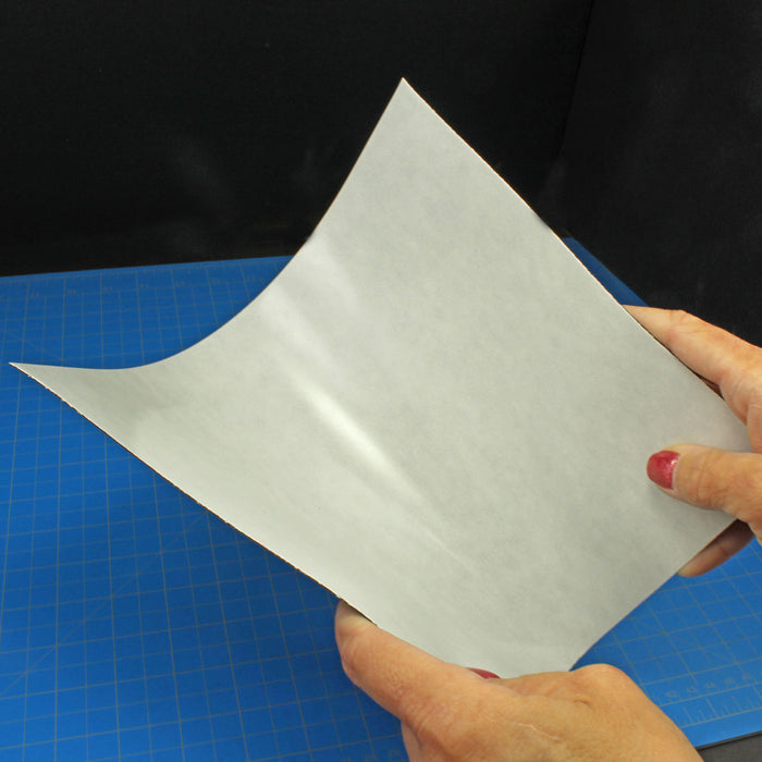 Two hands holding and slightly bending a flexible steel sheet over a blue hobby mat to demonstrate the material's flexibility.

