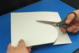 Close-up demonstration of cutting a thin white styrene sheet from the 0.030-inch Plasticard Pack using standard hobby scissors.