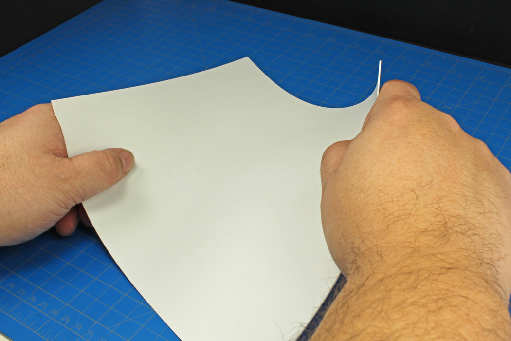 Hand demonstrating the flexibility of a thin 0.030-inch styrene sheet from the variety pack to show its suitability for curved model surfaces.