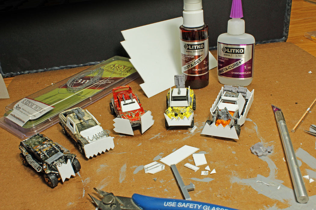 Custom Gaslands vehicle conversions in progress on a hobby bench using LITKO plasticard sheets, adhesives, and scissors to build miniature armor and ram plows.