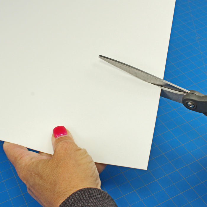 Close-up demonstration of cutting a thin white styrene sheet from the 0.060-inch Plasticard Pack using standard hobby scissors.